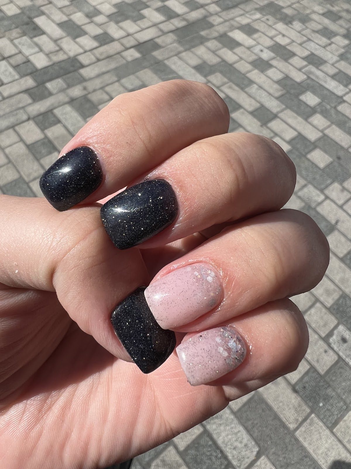 Hand seen from above with black glitter square nails and pale glitter accent fingers.