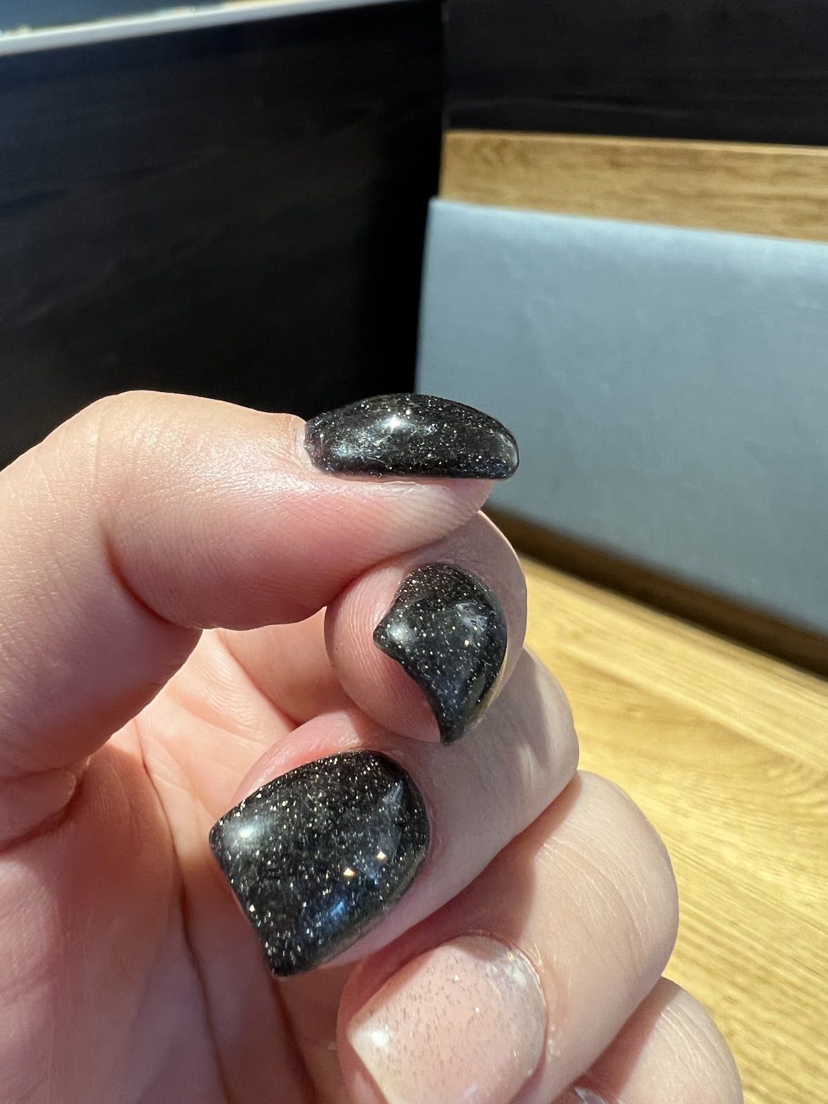 Curled hand on a café table, black glitter square nails catching the light.